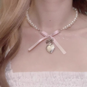 Detailed close-up of a pearl necklace featuring a pink silk bow and silver heart pendant