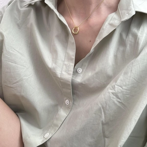 Detail of interlocking ring necklace pendant on a minimalist light green linen shirt