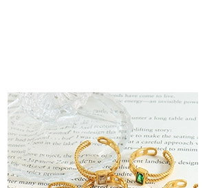 Detail of gold textured rings with emerald and clear zircon gems on vintage book pages
