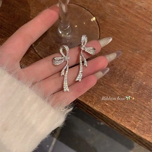 Detailed view of silver bow earrings with micro-paved zircons held by hand