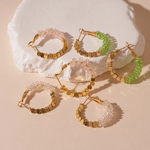 Créoles avec perles dorées et pierres de cristal colorées sur socle blanc texturé