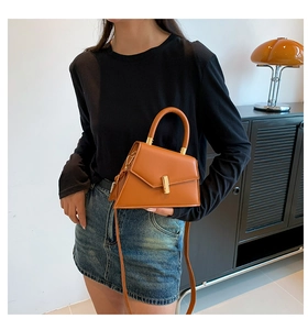 Chic brown leather handbag with gold clasp held by model in modern interior setting