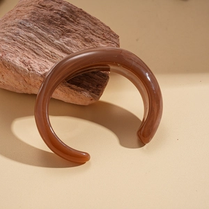 Detailed view of an amber acrylic open cuff bangle on a textured red stone background