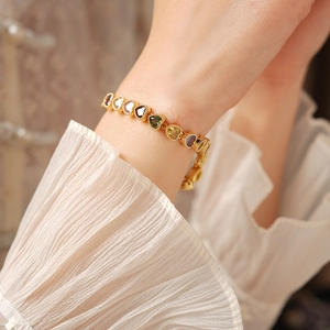 Detailed view of 18K gold plated heart bracelet with colorful gems on a female wrist