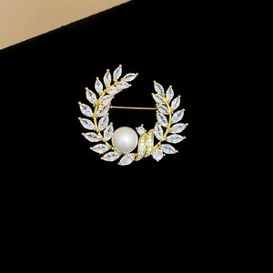 Close-up of golden wreath brooch with white pearl and marquise-cut sparkling zircons