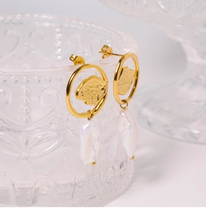 Detail of baroque pearl drop earrings with hammered gold rings on a vintage glass cup