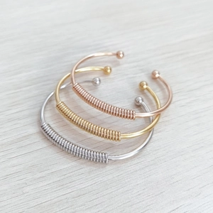 Polished stainless steel cuff bracelets in gold, silver, and rose gold with spring detail