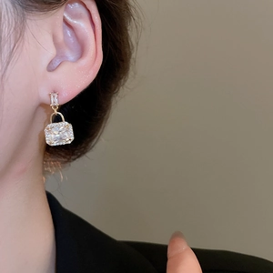 Close-up of golden square zircon earrings with a handbag design worn by a female model