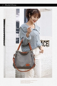 Detail of grey canvas crossbody bag featuring brown leather straps and logo patch
