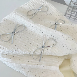 Dettaglio del tessuto plissettato bianco con pois neri e ornamento fiocco metallico
