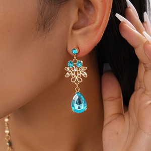 Macro shot of gold hollow flower earrings with teardrop blue stones and crystals