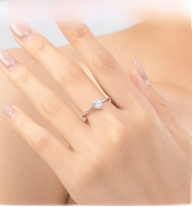Close-up of heart-cut cubic zirconia silver ring on finger with soft warm lighting
