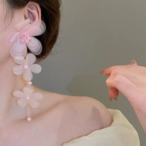 Detailed view of pink chiffon flower tassel earrings worn by a model on plain background