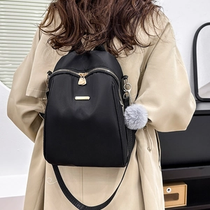 Detail view of black PU leather backpack with gold zippers and grey pompom charm