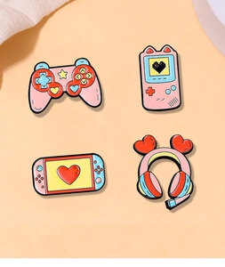 Close-up of four colorful enamel game consoles and headphone pins on orange background