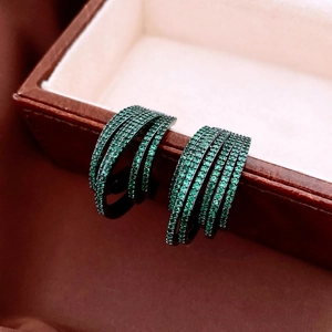 Détail macro de boucles d'oreilles multicouches avec zircons verts sur métal noir