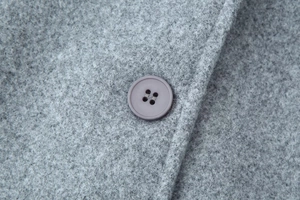 Detailed macro view of the purple resin button and wool blend fabric on a grey coat