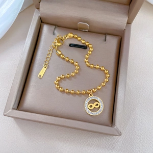 Macro detail of gold-plated infinity pendant with pavé crystals on a beaded chain