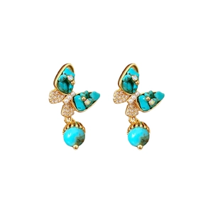 Boucles d'oreilles papillon plaquées or avec pierres turquoise et perles blanches sur fond blanc