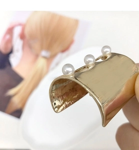 Detail of a U-shaped gold metal hair pin featuring three elegant pearls on the top curved edge