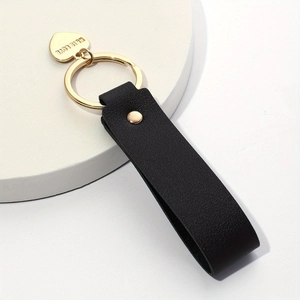 Detail of a black leather keychain with a gold heart pendant engraved with This Love