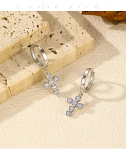 Macro shot of S925 silver hoop earrings with blue opal cross charms on travertine stone