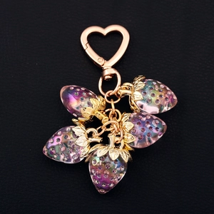 Detail of five translucent pink strawberry charms with golden heart clasp on leather