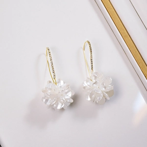 Detailed close-up of gold dangle earrings with white shell flowers and pavé crystals