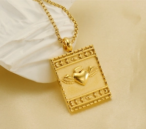 Macro view of gold square pendant with embossed winged heart and celestial symbols