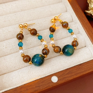 Détail de boucles d'oreilles créoles avec pierres œil de tigre et perles sur velours