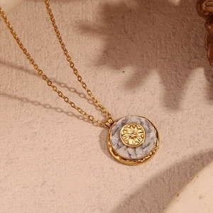 Detail of 18K gold plated necklace featuring a marble sunburst flower pendant on beige surface