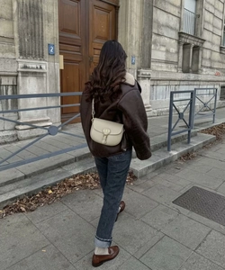 Gros plan du sac de selle ivoire avec boucle logo CD dorée et bandoulière en cuir