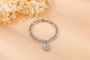 Silver stainless steel chain bracelet with Tree of Life coin pendant on beige background