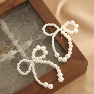 Detailed view of elegant bow earrings with imitation pearls on a silk background
