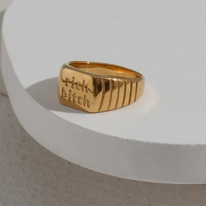 Detailaufnahme eines goldfarbenen Siegelrings mit der Gravur rich bitch in Gold