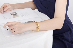 Detail shot of a minimalist gold stainless steel bangle with lock and key charms on a wrist