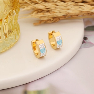 Elegant gold heart earrings with light blue gems and white crystals on ceramic tray