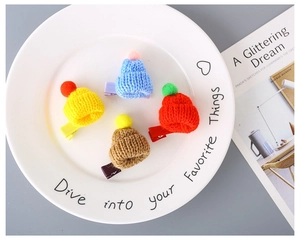 Detail of colorful mini knitted hat hair clips with pom-poms on a white ceramic plate
