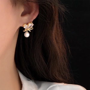 Détail d'une boucle d'oreille nœud en perle dorée avec zircons portée sur un mannequin