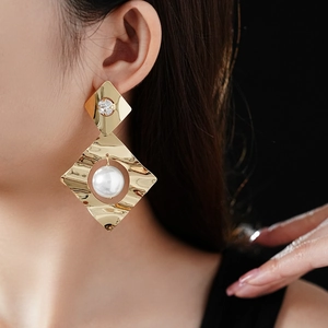 Detail view of geometric gold rhombus earrings featuring hammered metal and a large pearl
