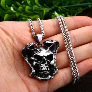 Nahaufnahme eines Punk-Edelstahl-Totenkopf-Anhängers mit Schlangen auf der Hand