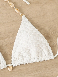 Detail of white textured bikini top featuring sea shell and pearl strap decorations