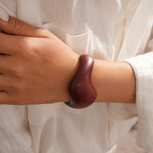 Close-up of a sculptural deep red acrylic open bangle on a model wearing white linen
