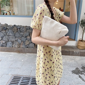Detailed close-up of a beige corduroy makeup bag held against a yellow floral dress