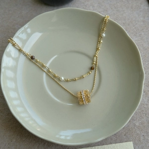 Detail of double-layer necklace with gold pendant, pearls and tiger eye stones in a ceramic dish