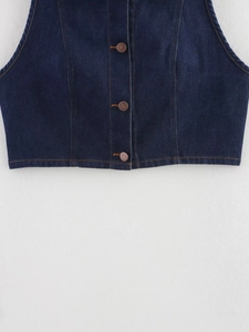 Détail du gilet en jean bleu foncé avec boutons en cuivre et coutures oranges