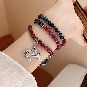 Close-up of three-layer beaded bracelet featuring red stones and silver elephant charm