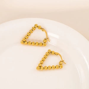 Golden V-shaped stainless steel beaded earrings on a white ceramic dish with warm lighting