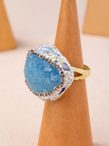 Détail de bague avec pierre brute bleu clair et cristaux sur support en bois