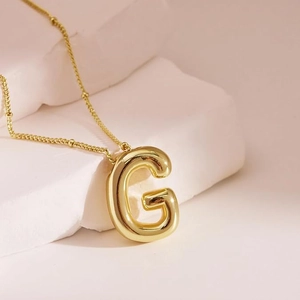 Macro detail of 18K gold balloon style letter G pendant on beaded chain necklace
